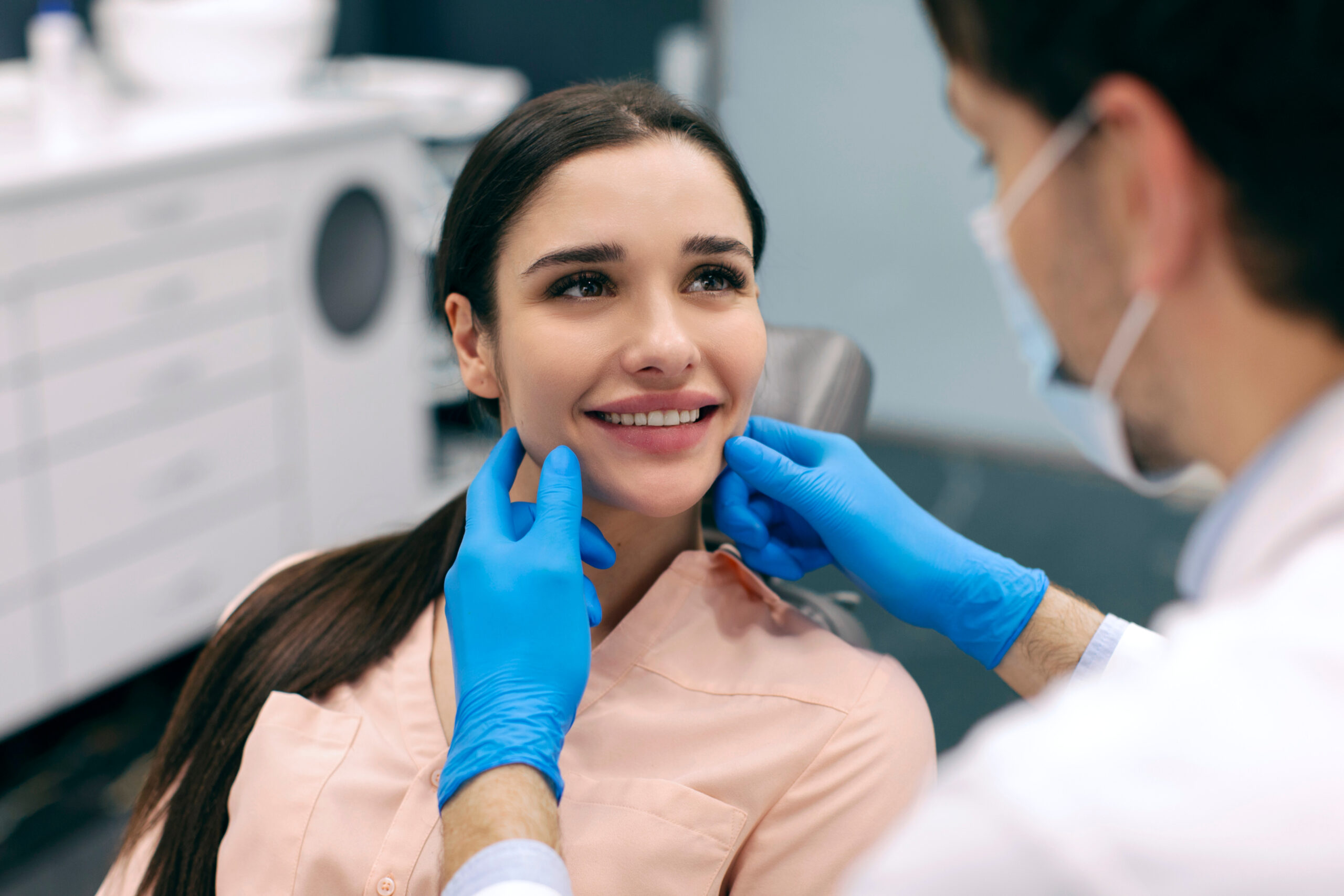 Dentist examining female patient during dental checkup while lady smiling, dental clinic office interior
