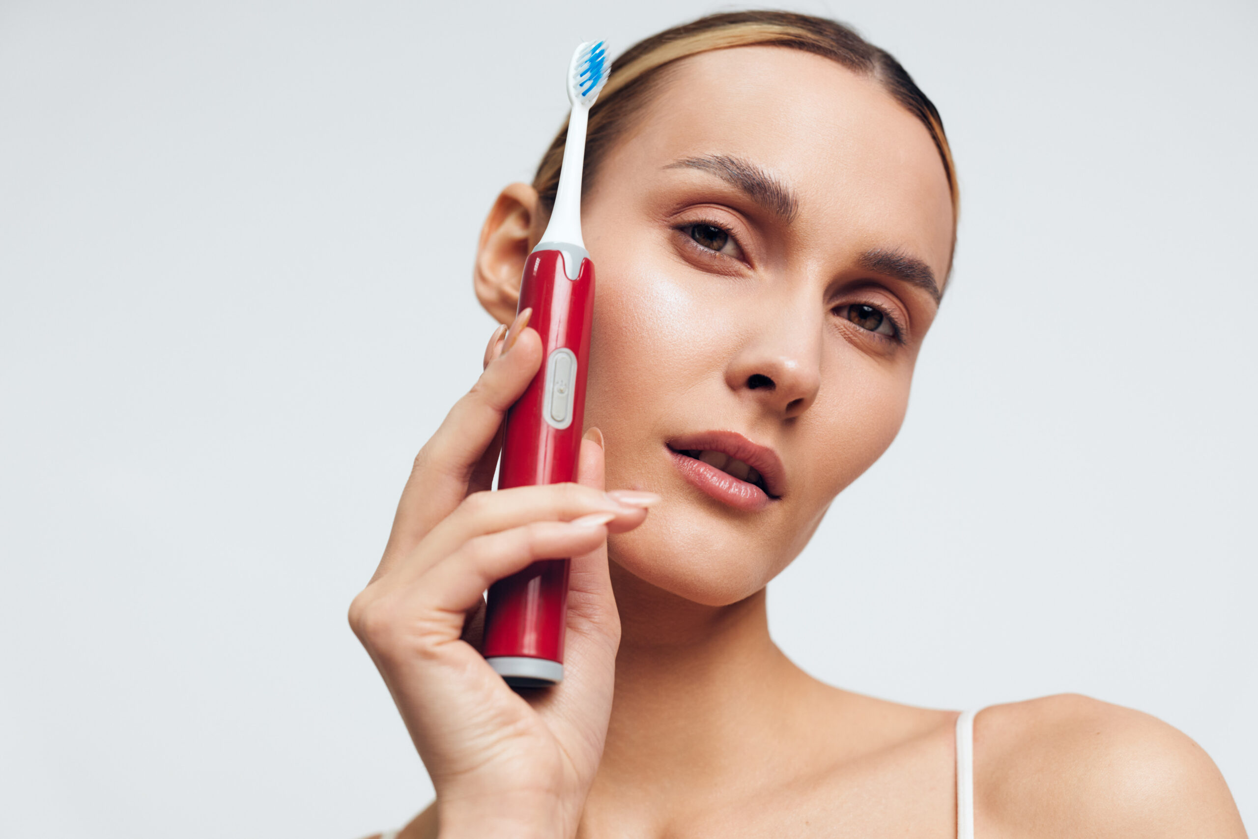 Portrait of a woman with a red electric toothbrush, emphasizing oral care, dental hygiene, and healthy habits in a fresh minimalist background with natural looking light.