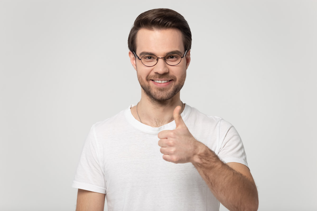 Happy Caucasian young man in glasses and white t-shirt isolated on grey studio background show thumbs up give recommendation, smiling male in spectacles look at camera recommend good service or deal