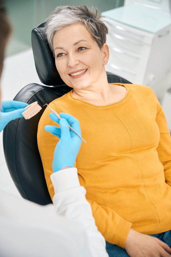 Smiling client of aesthetic dentistry clinic listening to male dentist who showing 3d model of her upper jaw and explaining oral hygiene, high quality dental care in relaxing environment
