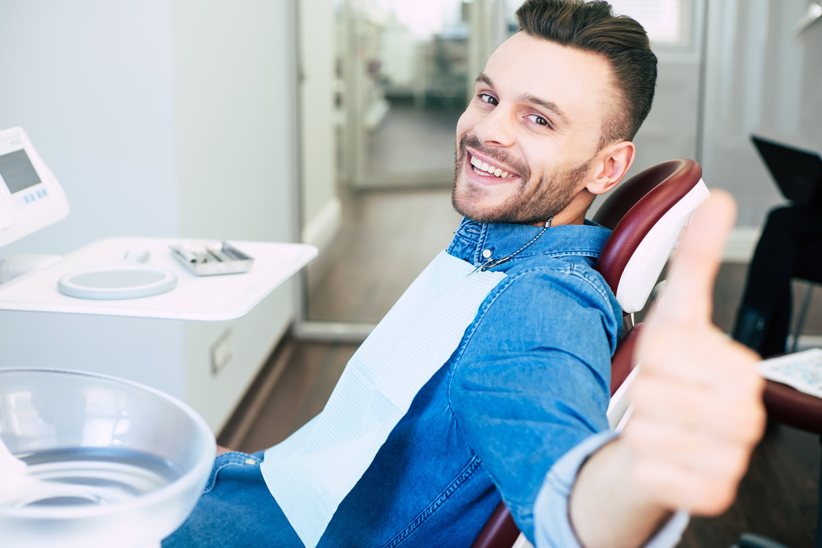 Wow! A dentist cabinet with all necessary supplement in it and a man in dental chair who is very happy about the result of a treatment that he got from the dentist.