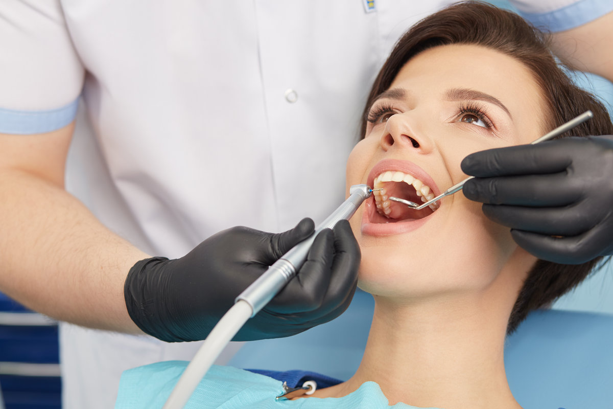 Young female patient visiting dentist office.Beautiful woman with healthy straight white teeth sitting at dental chair with open mouth during a dental procedure.Dental clinic.Stomatology.Dental caries prevention.