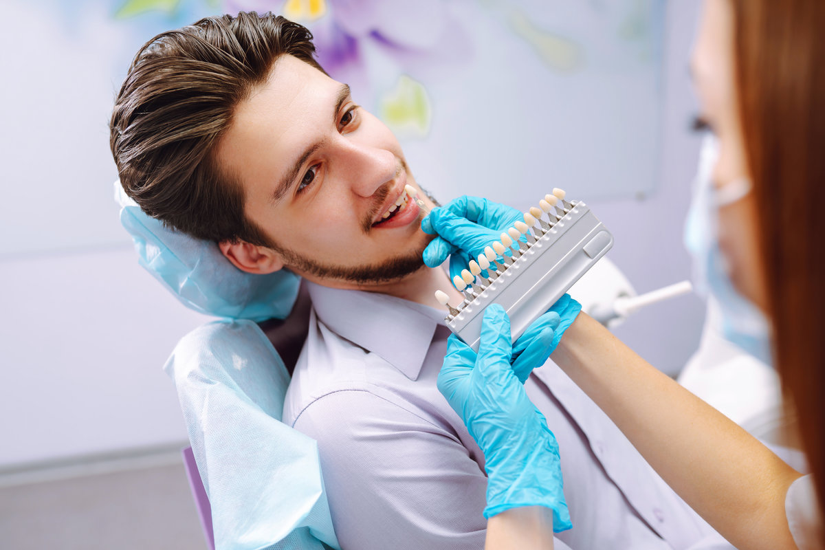 Young man at the dentist's chair during a dental procedure. Overview of dental caries prevention. Dentist examining patient's teeth in modern clinic. Healthy teeth and medicine concept.